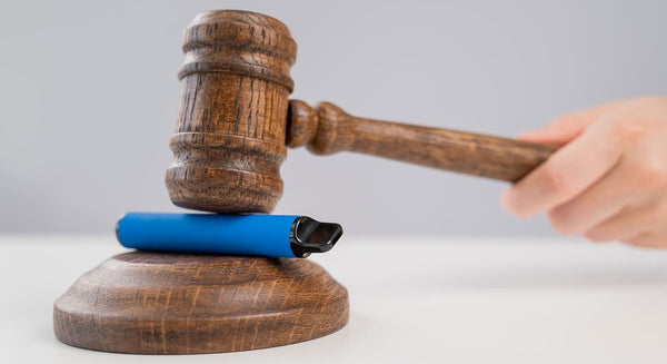 Disposable vape device on top of a wooden block being struck by a wooden gavel.