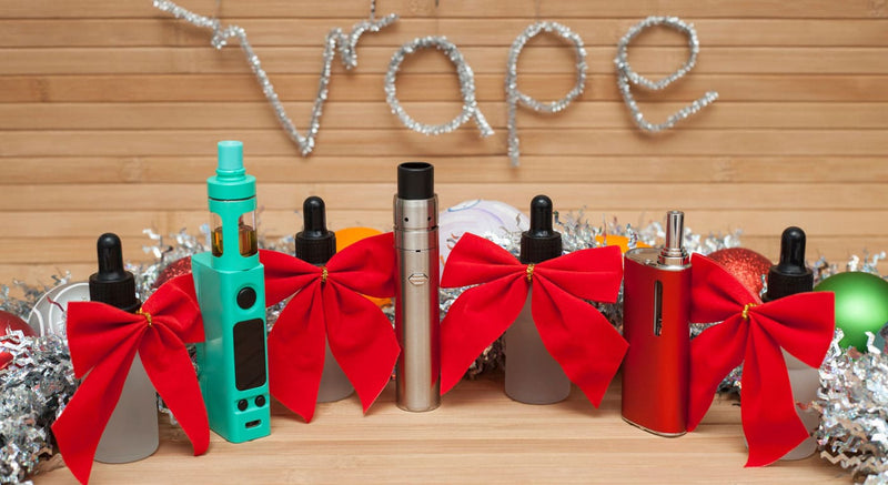 Vape gifts wrapped in bows and Christmas tinsel on wooden table.