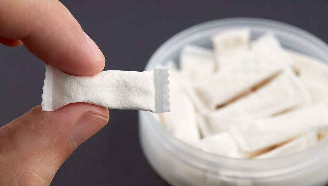 Person holding nicotine pouch with pack of pouches in the background.