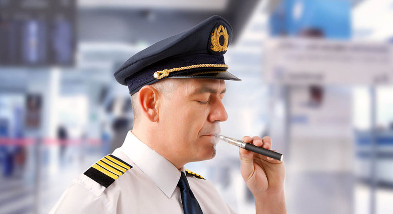 Pilot stood in an airport vaping on an electronic cigarette.