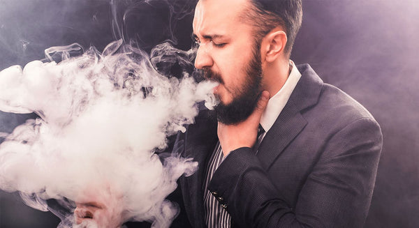 Man exhaling vapour from e-cigarette whilst holding his throat.